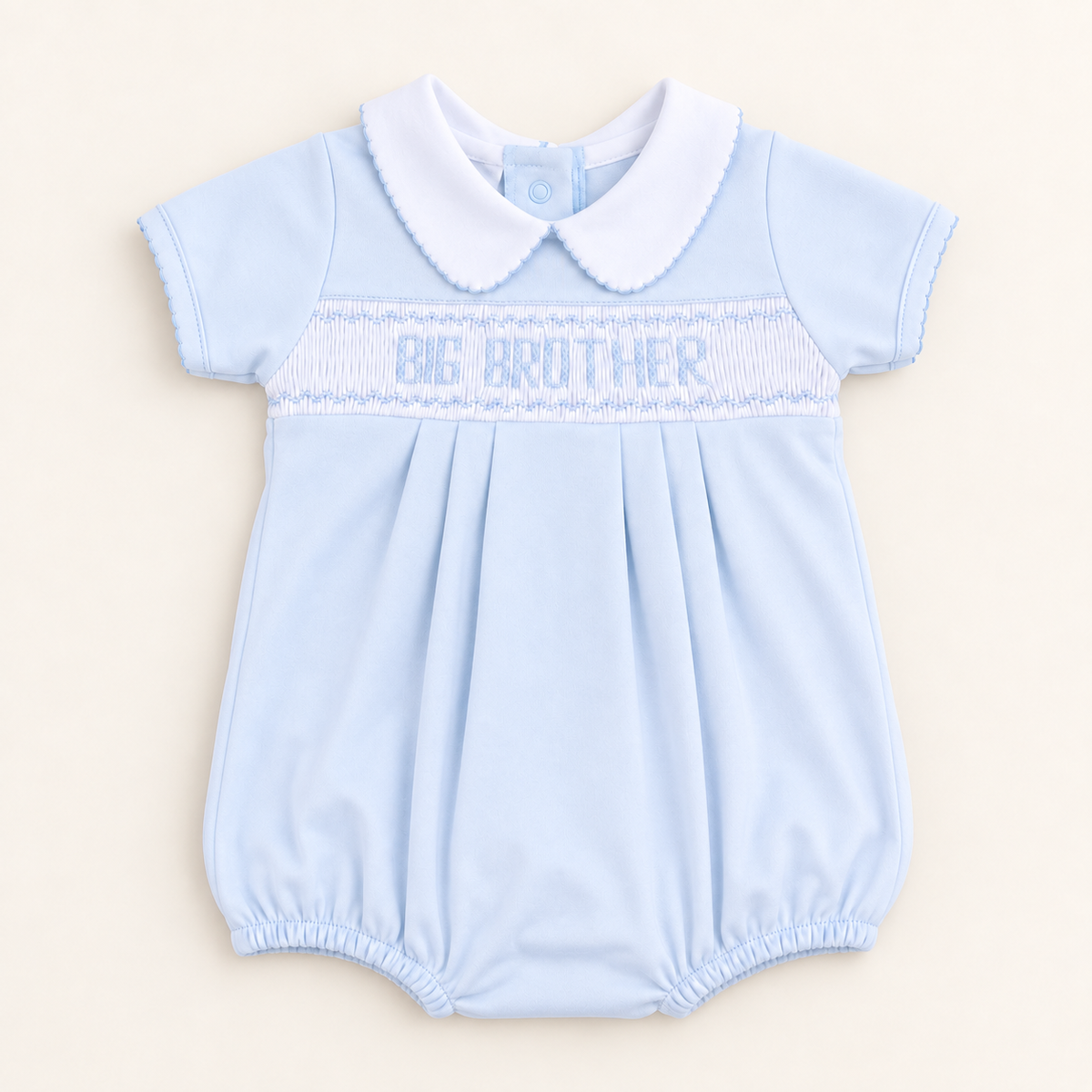 A light blue baby romper with a white Peter Pan collar and 'BIG BROTHER' smocked across the chest, laid flat on a warm cream background.