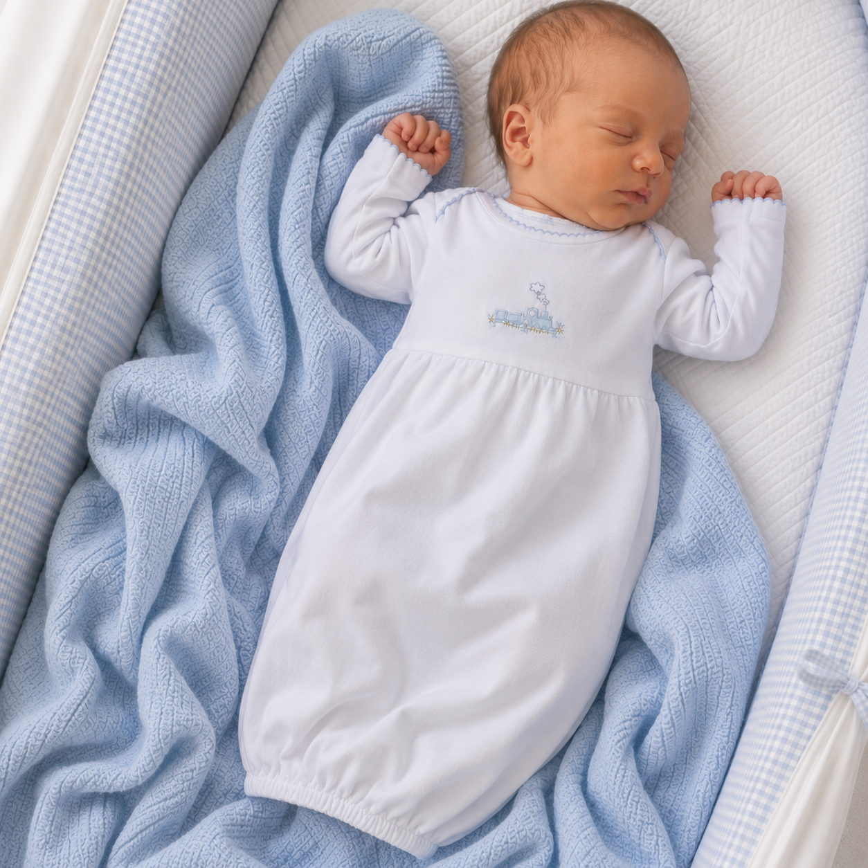 Newborn baby in a white hand embroidered gown  with blue train embroidery lying on a blue blanket.