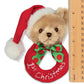 Teddy bear rattle wearing a red '1st Christmas' wreath with a Santa hat, next to a ruler for scale.