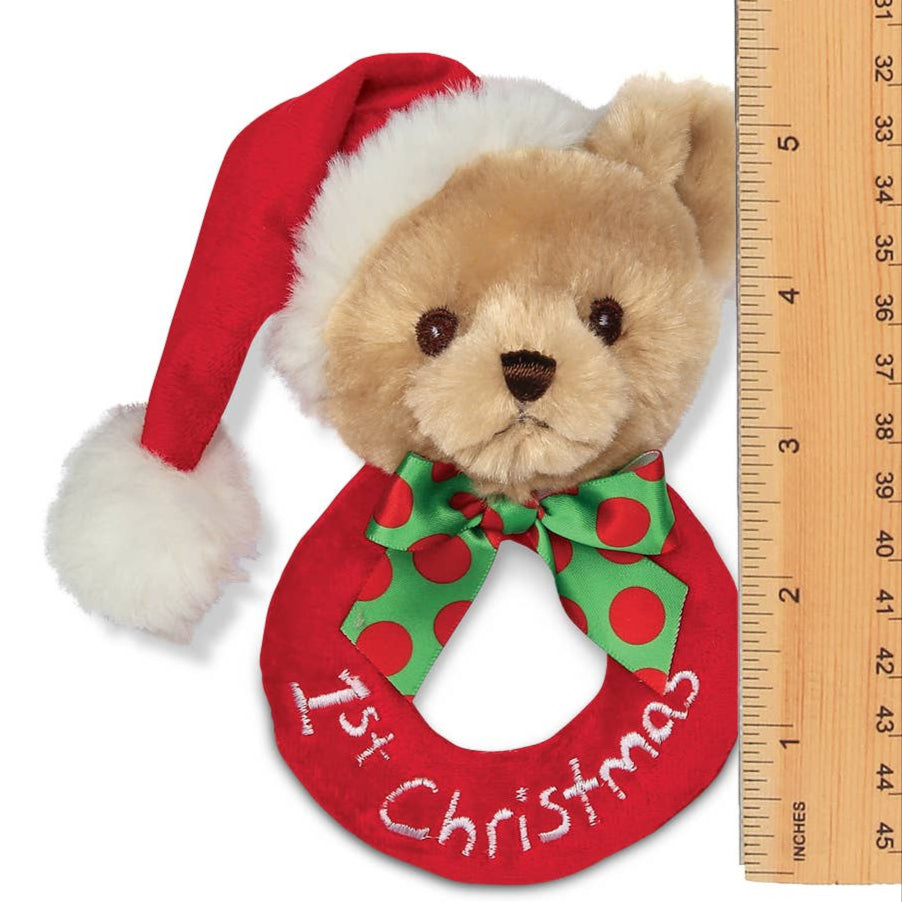 Teddy bear rattle wearing a red '1st Christmas' wreath with a Santa hat, next to a ruler for scale.