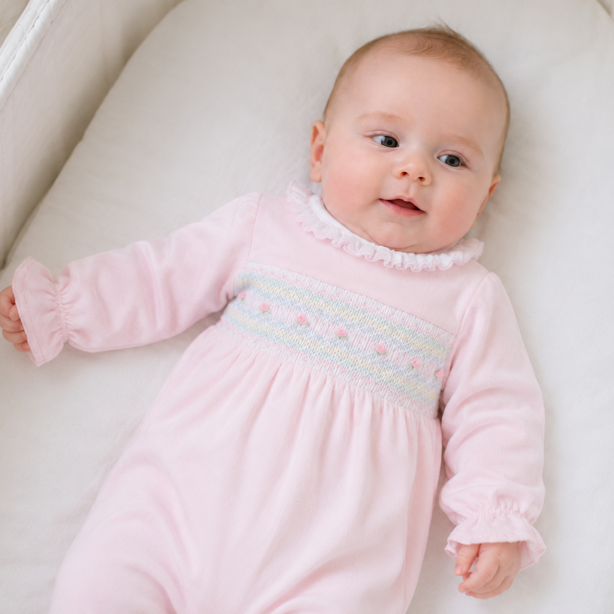 baby girl in a white bassinet wearing a magnolia baby smocked pima pink footie