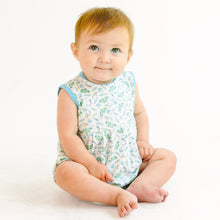  Baby sitting on a white background wearing a fishing patterned romper.
