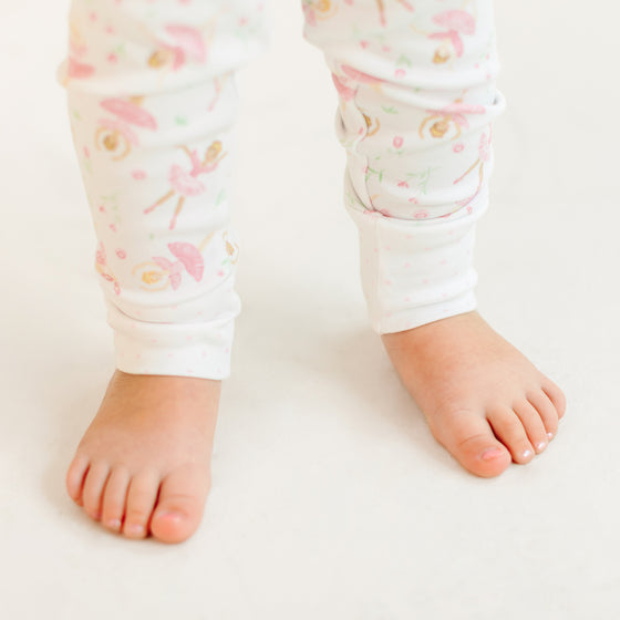 Baby legs wearing white pants with floral ballerina pattern on a light background