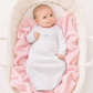 Baby in a white hand embrdoiered lgown by magnolia baby ying on pink blankets in a white bassinet