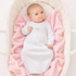 Baby in a white hand embrdoiered lgown by magnolia baby ying on pink blankets in a white bassinet