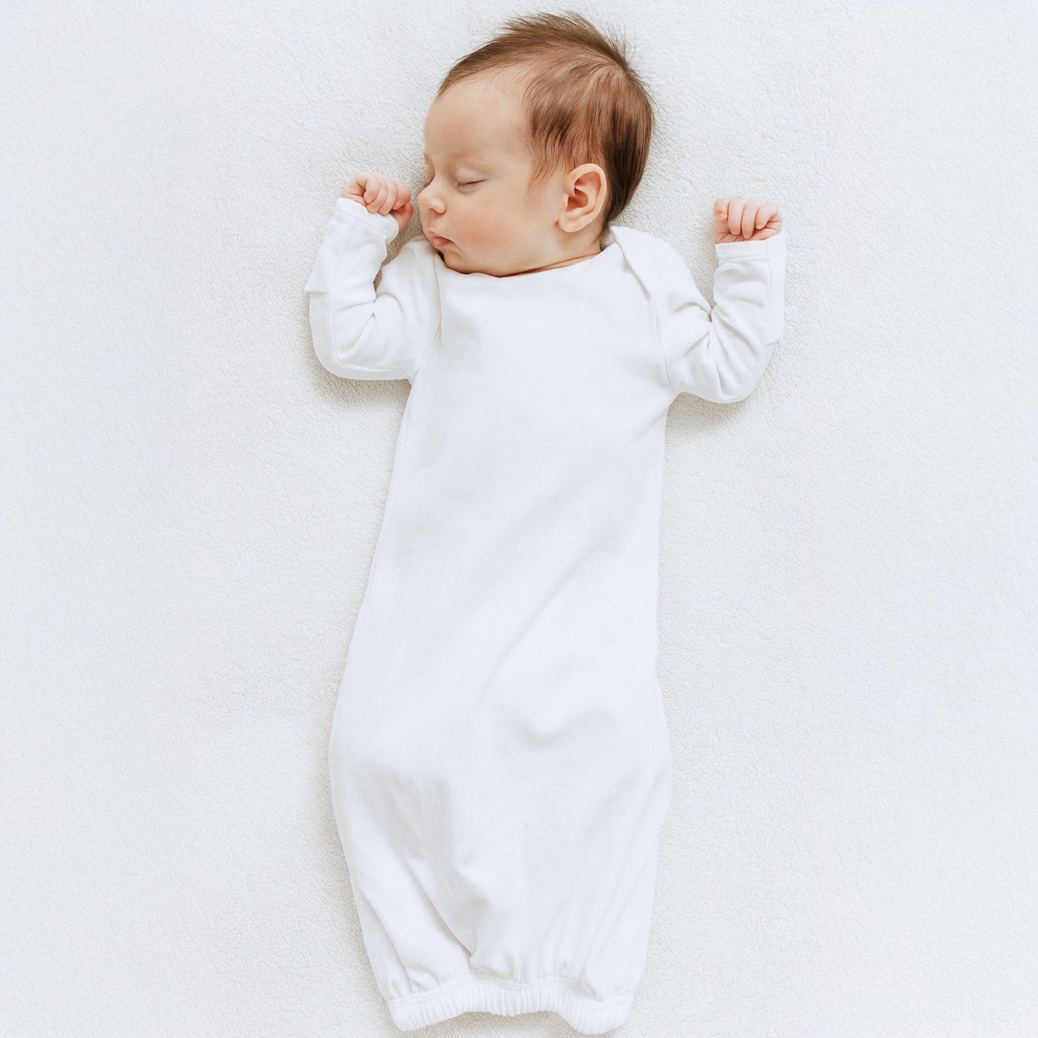 Baby in a white lap gown lying on a white surface