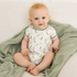 A baby sitting on a soft green muslin blanket, wearing a white short-sleeve bodysuit with a mallard duck print and green trim.